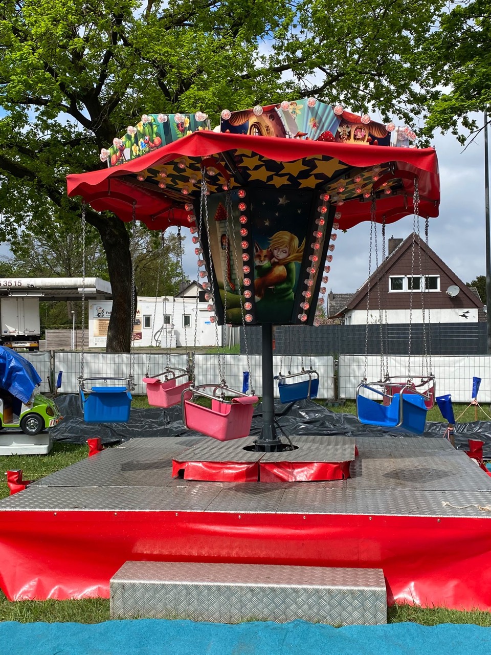 Kinderkettenkarussell mit rotem Dach und bunten Sitzen im Freien