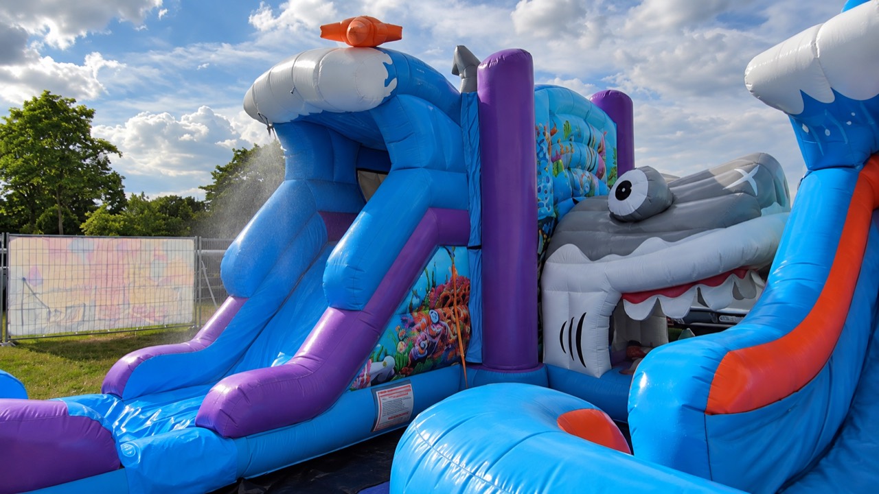 Blaue aufblasbare Wasserrutsche mit lila Bahnen und großem Hai-Motiv